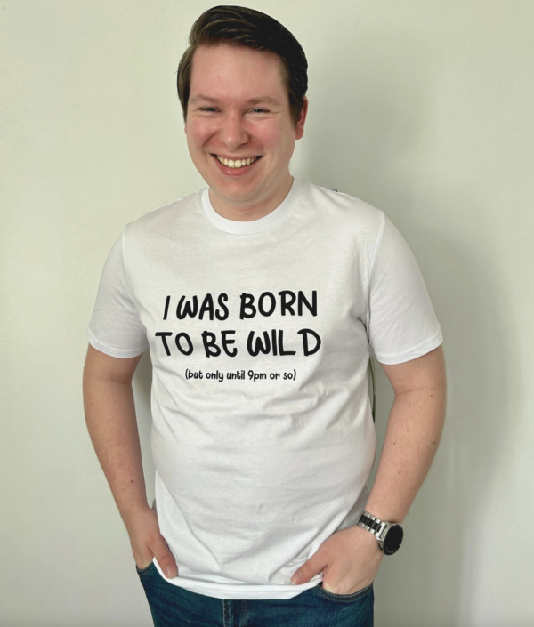 Man wearing white t-shirt that says 'I was born to be wild, but only until about 9pm or so' laughing - wider shot