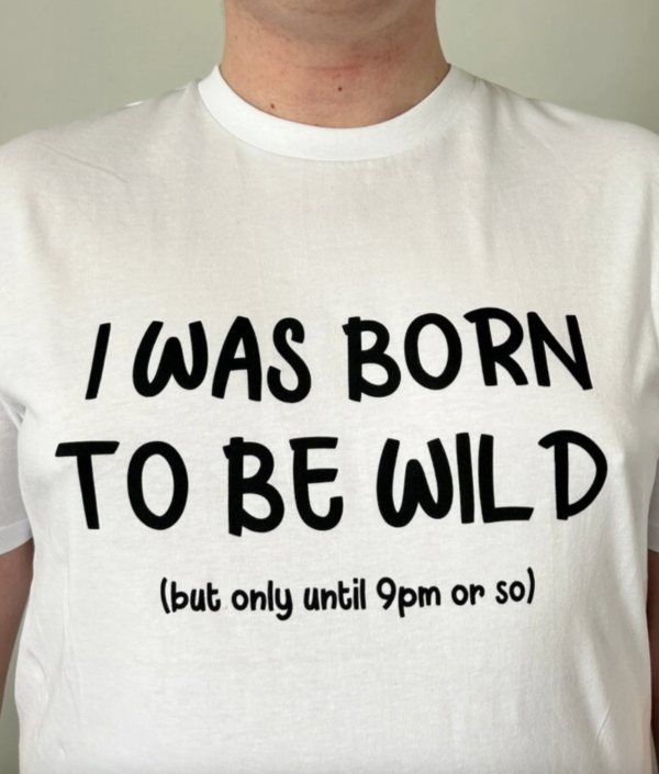 Zoomed in shot of white t-shirt with 'I was born to be wild, but only until about 9pm or so' on it