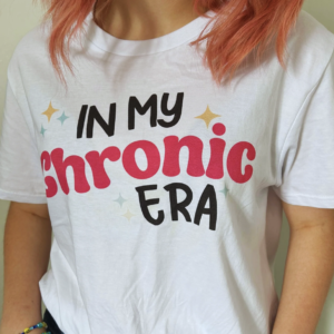 Woman with pink hair wearing a white t-shirt that says 'In My Chronic Era'